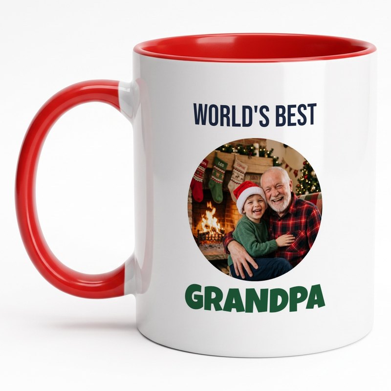 A red-rim "World's Best Grandpa" mug with a grandfather and grandson in a Santa hat by the fireplace