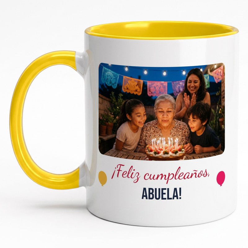 A yellow-rim "¡Feliz cumpleaños, abuela!" mug with a grandmother blowing out candles on a tres leches cake with her grandkids